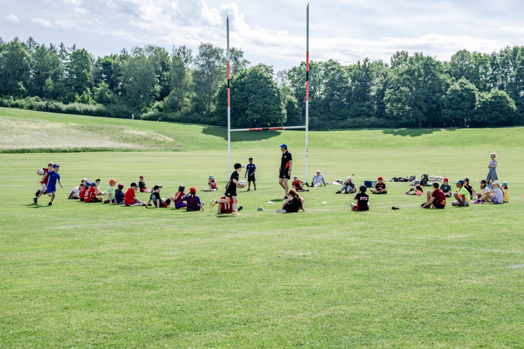 Kinder spielen Rugby auf der grossen Allmend mit einem Trainer