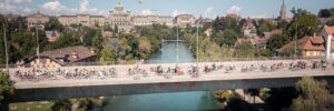 Velofahrende auf einer Brücke in der Stadt Bern, im Hintergrund das Bundeshaus und die Aare