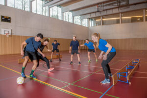 Erwachsene spielen Bänklifussball in einer Turnhalle