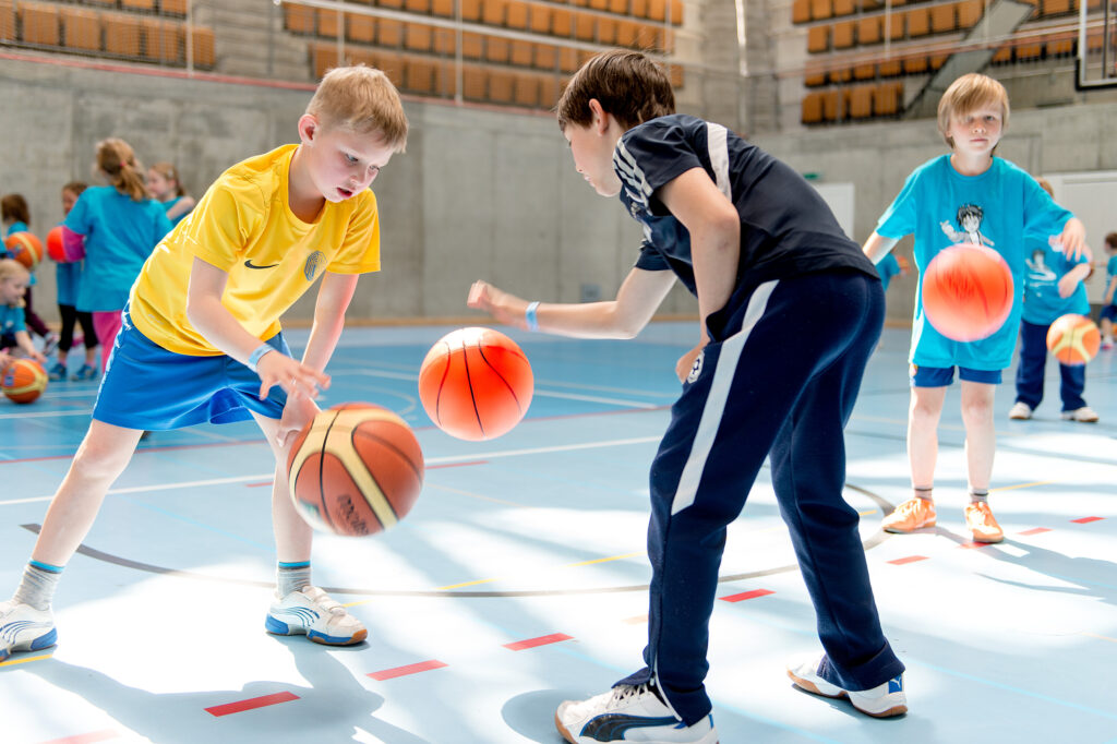 Zwei Jungen prellen Basketbälle in einer Turnhalle